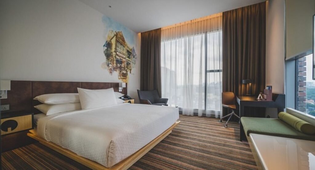 Beach hotel bedroom look with layered white bedding, woven bench, simple green plant, and coastal gallery ledge shelf