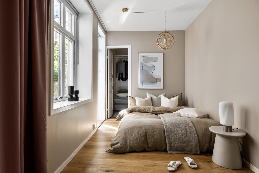 Lake house bedroom with white bedding, soft blue accent pillows, light wood furniture, and calm water-inspired interior style.