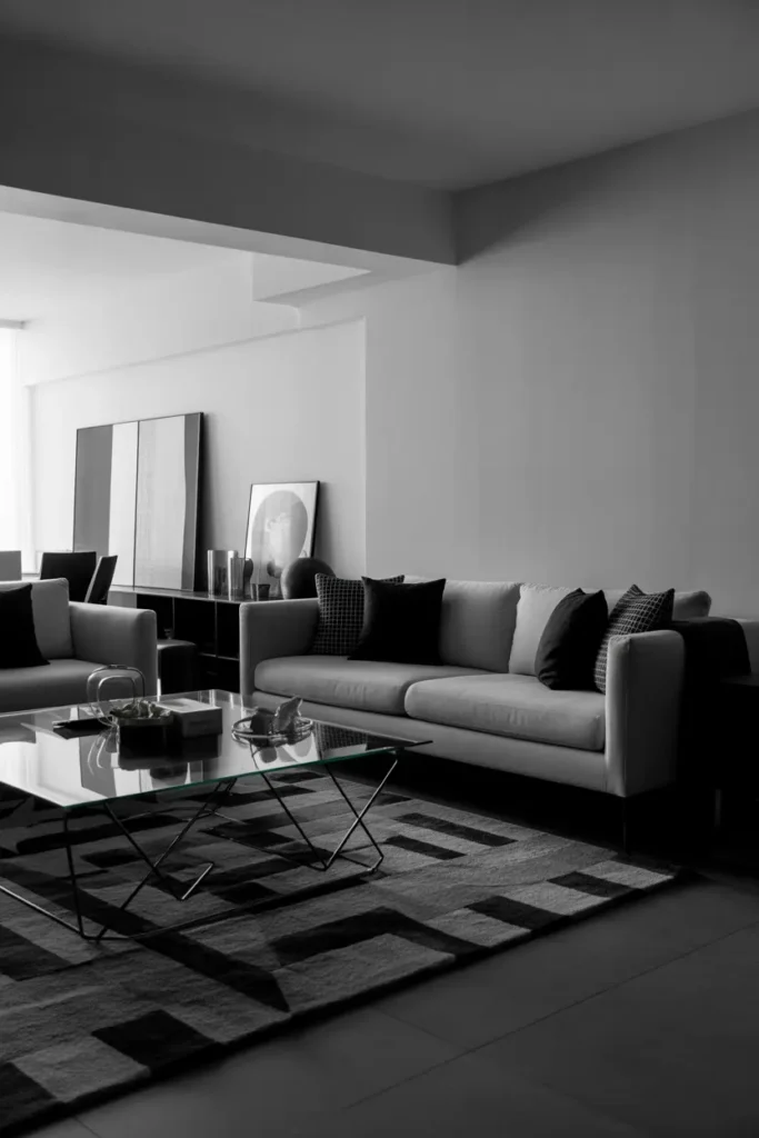  Modern monochrome living room with black and white color palette, soft diffused lighting, sleek sofa, geometric patterned rug, glass coffee table, minimal wall art, high contrast decor, clean lines, contemporary aesthetic, balanced composition, wide shot highlighting contrast, textures, and structured layout in a stylish apartment setting.